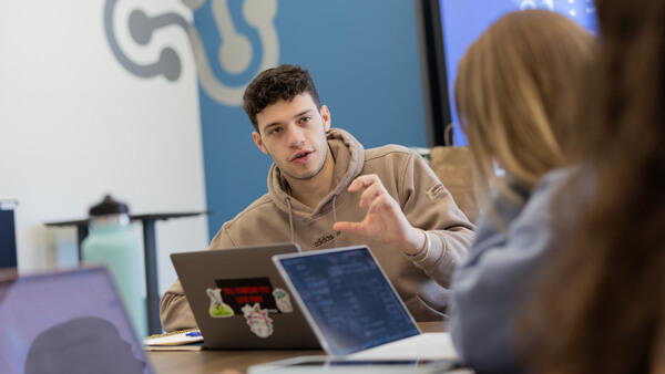 A male student talking to other students sitting at a table